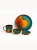 A vibrant ceramic tableware set with a glossy, colorful reactive glaze is arranged against a solid white background. The collection includes a large artistic plate with orange and teal patterns, a matching mug, a medium bowl, and a small saucer.