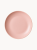 A top-down view of a matte, pastel pink ceramic plate.